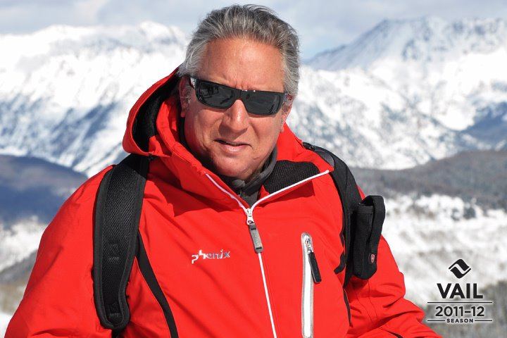 Giora Gilead con chaqueta roja de esquí y gafas de sol, ante montañas nevadas